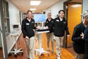 Three ܽƵ students push a cart through the a hospital hallway.